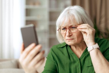 Üst düzey kadın akıllı telefon ekranına bakarken gözlük ayarlıyor. Olgun Kafkas kadın okuma metni veya mobil aygıt bilgileri kontrol