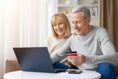 Üst düzey çift evde dizüstü bilgisayar ve kredi kartıyla online ödeme yapıyor. Ekommerce, dijital bankacılık ve teknoloji kullanımını temsil eden online alışveriş yaparken elinde kart tutan olgun bir adam