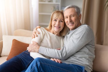 Son sınıf çifti evdeki kanepede rahatça gülümsüyor. Olgun erkek ve kadın evde huzurlu vakit geçiriyorlar. Aile mutluluğunu, emeklilik yaşam tarzını ve aile rahatlığını temsil ediyorlar.