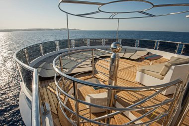 Büyük lüks bir yatın kıç güvertesinde güneşli koltuklar kanepe ve tropikal deniz manzaralı arka plan.