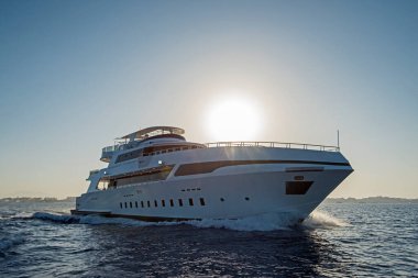 Günbatımında pruva dalgalı tropikal denizde lüks bir özel motor yatı sürüyor.