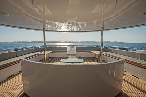 Teak stern wooden deck of a large luxury motor yacht with chairs sofa table and tropical sea view background