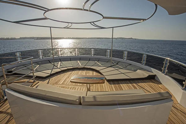 Teak stern deck of a large luxury motor yacht with sunbeds chairs sofa table and tropical sea view background