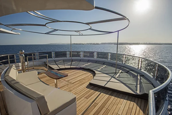 有日光浴椅沙发桌子和热带海景背景的大型豪华游艇的纤细船尾木制甲板 — 图库照片