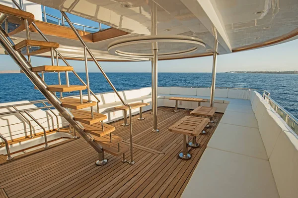 Teak stern wooden deck of a large luxury motor yacht with chairs sofa table and tropical sea view background