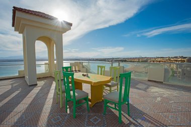 Lüks bir tropikal otel tesisinde çatı katında yemek masası ve sandalyeler.