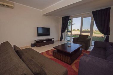 Lüks apartmandaki oturma odasının oturma odası teras kapısı ve bahçe manzarası ile döşenmiş iç tasarım dekorasyonunu gösteriyor.