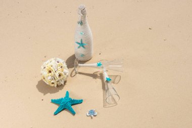 Tropikal ada kumsal cennetinde şampanya şişesi ve şarap kadehleriyle romantik düğün süslerinin yakın çekimi.