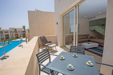 Tropikal tatil köyündeki lüks bir dairenin teras mobilyaları ve yüzme havuzu manzarasının üzerinde sandalyeler.