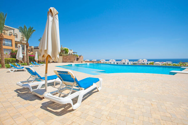 Большой открытый бассейн на роскошном тропическом курорте с шезлонгами