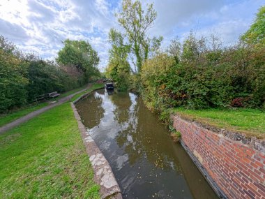 İngiliz kırsal kesimlerinde mavi gökyüzü ve sonbahar mevsiminde yansıması olan İngiliz su yolu kanalı boyunca seyahat eden dar bir kayığın görüntüsü