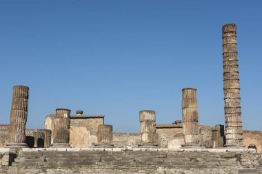 Terk edilmiş antik Roma şehir tapınağındaki sütunların kalıntıları mavi gökyüzü arka planıyla iç kısımları harabeye çeviriyor.