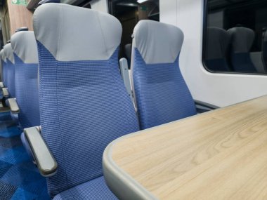 Boş bir banliyö vagonunda, içi boş koltuklar ve masalarla dolu bir iç mekan.