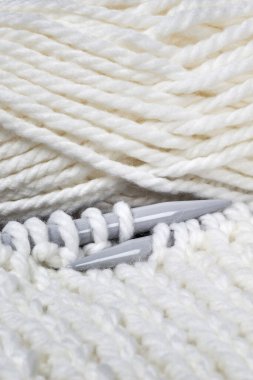 Örgü ipliği topun yanında yatar, renk beyazdır, iplik yumuşak bir yapıya sahiptir, büyük ve gri örgü iğneleri örer; düz yatak, yakın çekim