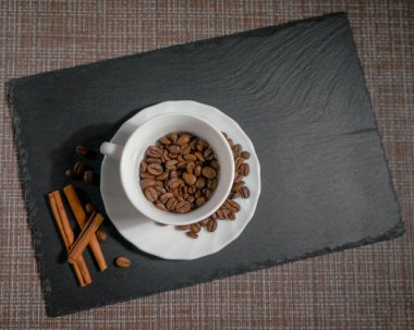 Beyaz seramik fincanda tarçın çubukları olan kavrulmuş kahve çekirdeği.