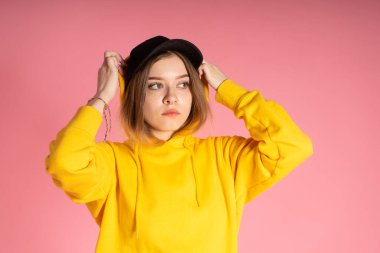 Sarı kapüşonlu, siyah şapkalı, burnu delinmiş, kapüşonlu, yakın plan bir kadın.