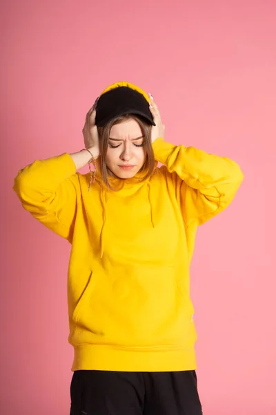 Sarı kapüşonlu ve siyah şapkalı bir kız başını tutuyor. Anlaşılan korkunç düşünceleri ya da baş ağrısı varmış.