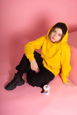 Kapüşonlu ve siyah şapkalı bir kadın kağıt bardağın yanında aşk ve gökkuşağı renkli bir kalp yazar.