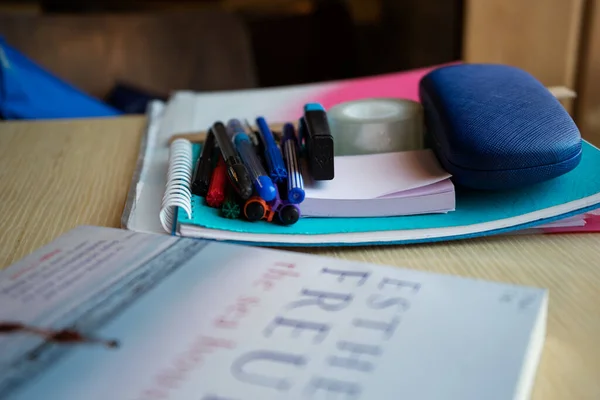 there are many pens and felt-tip pens on the table, they are on a notebook, in front of them is a blurry book