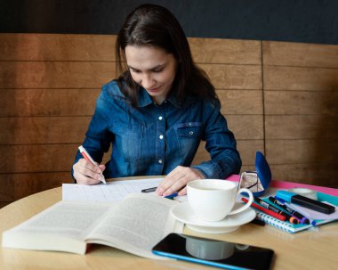 Gülümseyen bir kız duygularının programı düzeltir. Önünde yeşil çay, akıllı telefon, gözlük, farklı işaretler, yapıştırıcı bant, defter ve beyaz bir kupa vardır.