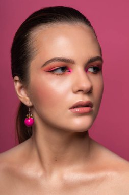 Harika profesyonel makyajlı, pembe küpeli, uzun kahverengi saçlı güzel bir genç kızın yüksek güzellikte fotoğrafı. Pembe arka planda poz vermek. Yakın plan. Stüdyo çekimi. Portre