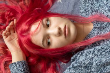 Mavi kazaklı, zarif ve parlak saçlı pembe saçlı bir kız beyaz yıldızlı mavi bir peçede yatıyor. Kıvırcık saçlı güzel bir model kadın. Bakım ve güzellik saç ürünleri