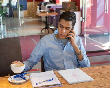 Önemli bir sözleşme imzaladıktan sonra, genç işadamı lezzetli bir kahve içer. Mavi bir kot gömlek ve güzel bir kol saati giyiyor. Kafeteryada.