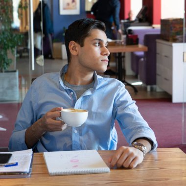 Önemli bir sözleşme imzaladıktan sonra, genç işadamı lezzetli bir kahve içer. Mavi bir kot gömlek ve güzel bir kol saati giyiyor. Kafeteryada.