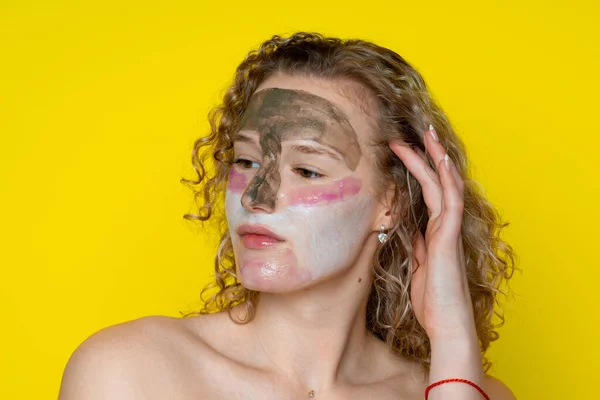 Kıvırcık saçlı ve yüzünde çıplak omuzları olan kadın üç çeşit kozmetik maske takıyor, kadın yüz bakımını yapıyor, sola bakıyor, stüdyoda, sarı arka planda.
