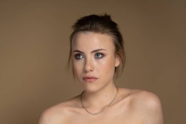 Heterokromi, kısa saç, iyi makyaj, göz kalemi, soluk ten ve piercingli genç bir modelin portresi. Sola bakıyor. Feminizm ve Güçlendirme. Bej arkaplan çekimleri