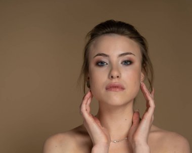 Heterokromisi olan genç bir modelin portresi, yüzüne dokun, kısa saçlı, iyi makyajlı, soluk tenli, piercingli. Önüne bak. Feminizm ve Güçlendirme. Bej arkaplan