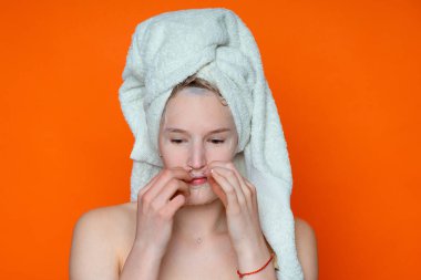 İyileştirmek, temizlemek, cildini geliştirmek için kozmetik maskeli genç, düşünceli güzel bir kız elleriyle yüzüne dokunuyor, aşağı bakıyor, ıslak saçlar ve beyaz bir havlu, kıvırcık saçlı, kırmızı arka plan.