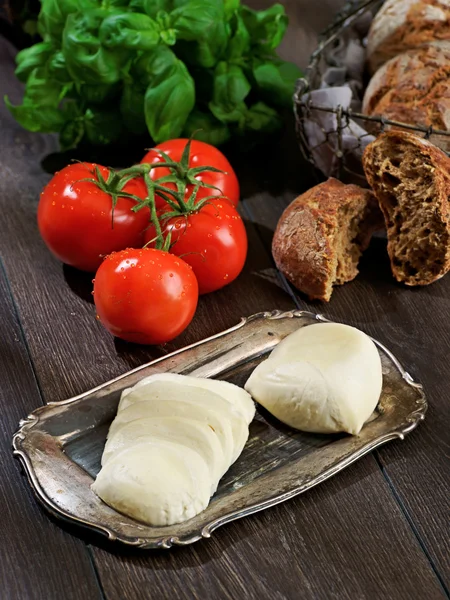 Mozzarella, tomatoes, bread, basil, composition on a wooden table — Stock Photo, Image
