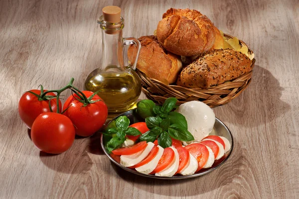 Mozzarella, tomatoes, olive, basil, roll, composition on a wooden table — Stock Photo, Image