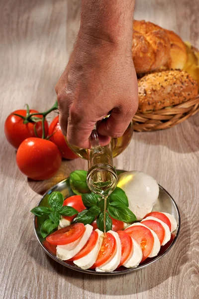 Mozzarella, tomatoes, olive, basil, roll, human hand pouring olive from a bottle — Stock Photo, Image