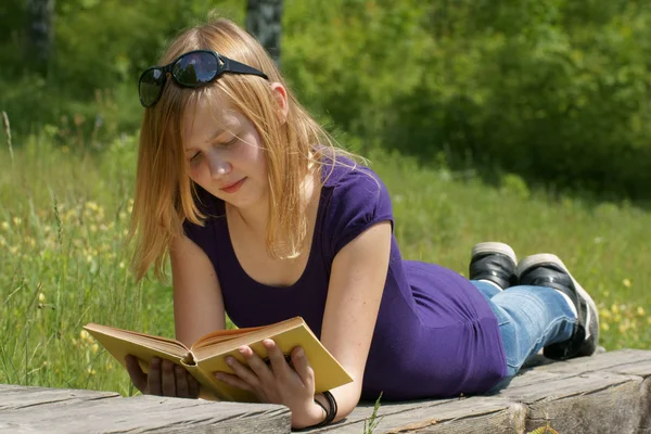 Ung flicka läser en bok i parken — Stockfoto