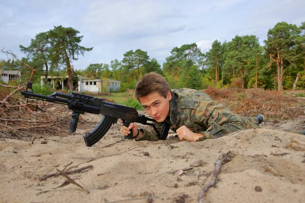 Tiener, jongen kruipen in uniform en met een geweer, zachte luchtpistool — Stockfoto