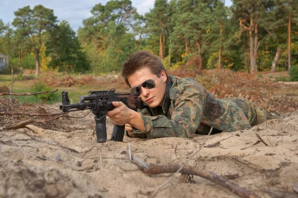 Tiener, jongen liggen in zijn strijd jurk, zonnebril en een geweer, zachte luchtpistool — Stockfoto