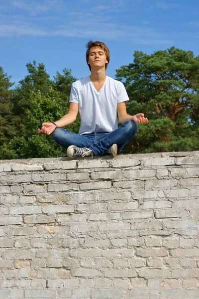 Adolescente, menino sentado em uma parede e medita — Fotografia de Stock