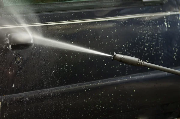 Limpiador de agua de alta presión de primer plano como se ve rociando en la puerta del coche azul oscuro con rastros de jabón — Foto de Stock