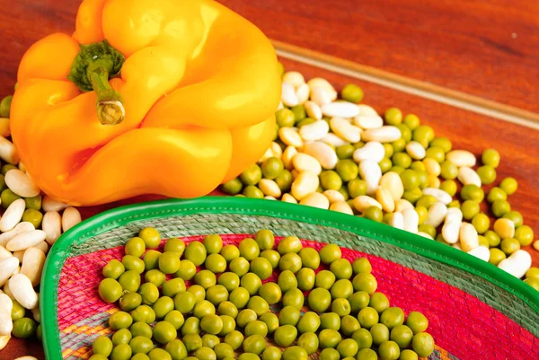 Peeled and unpelaed green lima beans mixed with orange capsicum on wooden surface — Stock Photo, Image