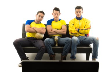 Üç arkadaş sarı giyen koltukta oturan spor tv arkasından ateş konsantre yüz ifadeleri, beyaz arka plan ile televizyon izlerken gömlek