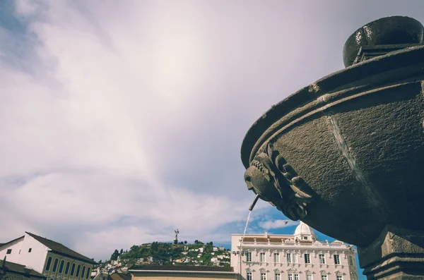 Fuente de piedra en medio del cielo azul, edificio antiguo en la parte posterior y panecillo virgen —  Fotos de Stock