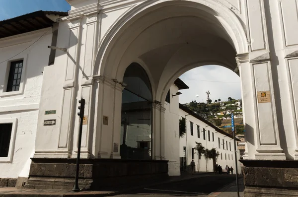 Gran arco blanco en el centro de la sreet, museo de la ciudad en un lado. Colina con virgen detrás — Foto de Stock