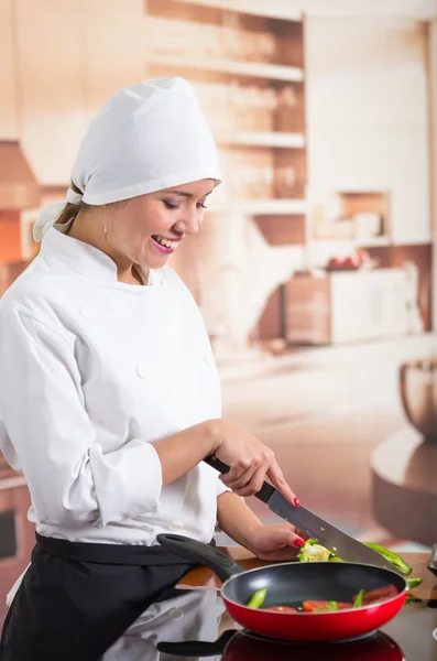 Köchin steht lächelnd am Tresen und schneidet Gemüse neben roter Pfanne — Stockfoto