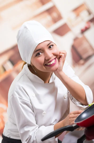 Bonito retrato de mujer chef con traje de cocina apoyado en el mostrador de la cocina sonriendo a la cámara —  Fotos de Stock