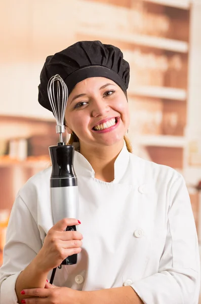 Női szakács visel főző ruhát pózol boldogan gazdaság elektromos kézi turmixgép — Stock Fotó