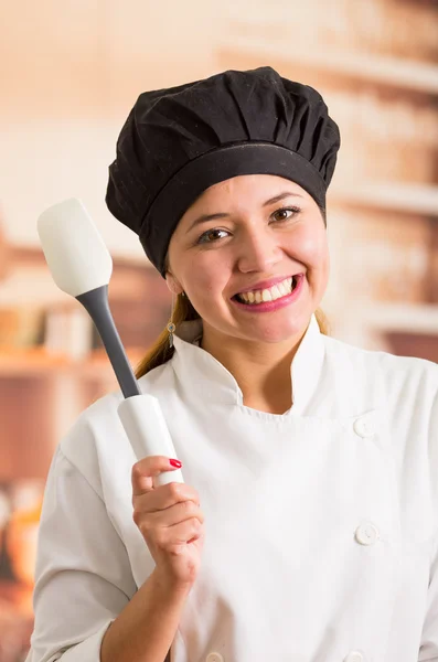 Mujer chef con traje de cocina posando alegremente sosteniendo espátula de plástico blanco —  Fotos de Stock