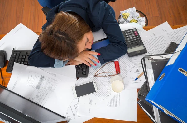 Giovane donna seduta e sdraiata addormentata sulla scrivania con documenti, calcolatrice, penne, tastiera del computer — Foto Stock