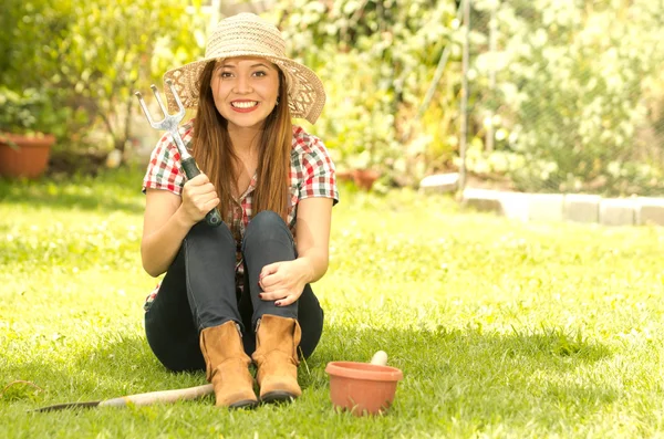 Young woman sitting on grass holding gardening tools smiling to camera — Stock Photo, Image